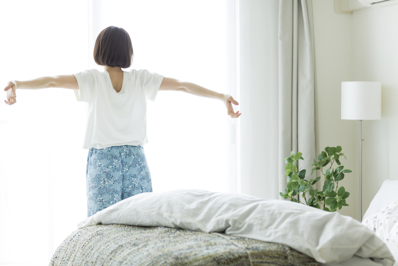 カーテンを開け朝日を浴びる女性