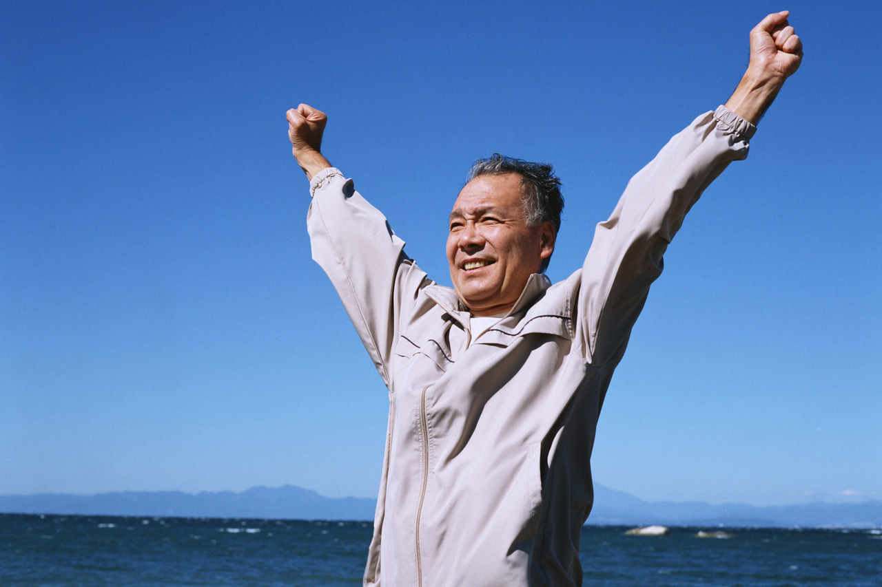 青い空と海を背景に伸びをする男性