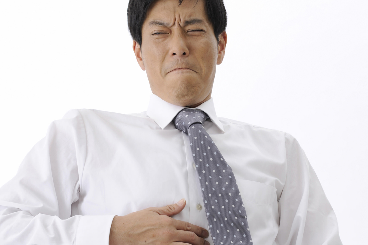 胃を押さえ顔をしかめるビジネスマン