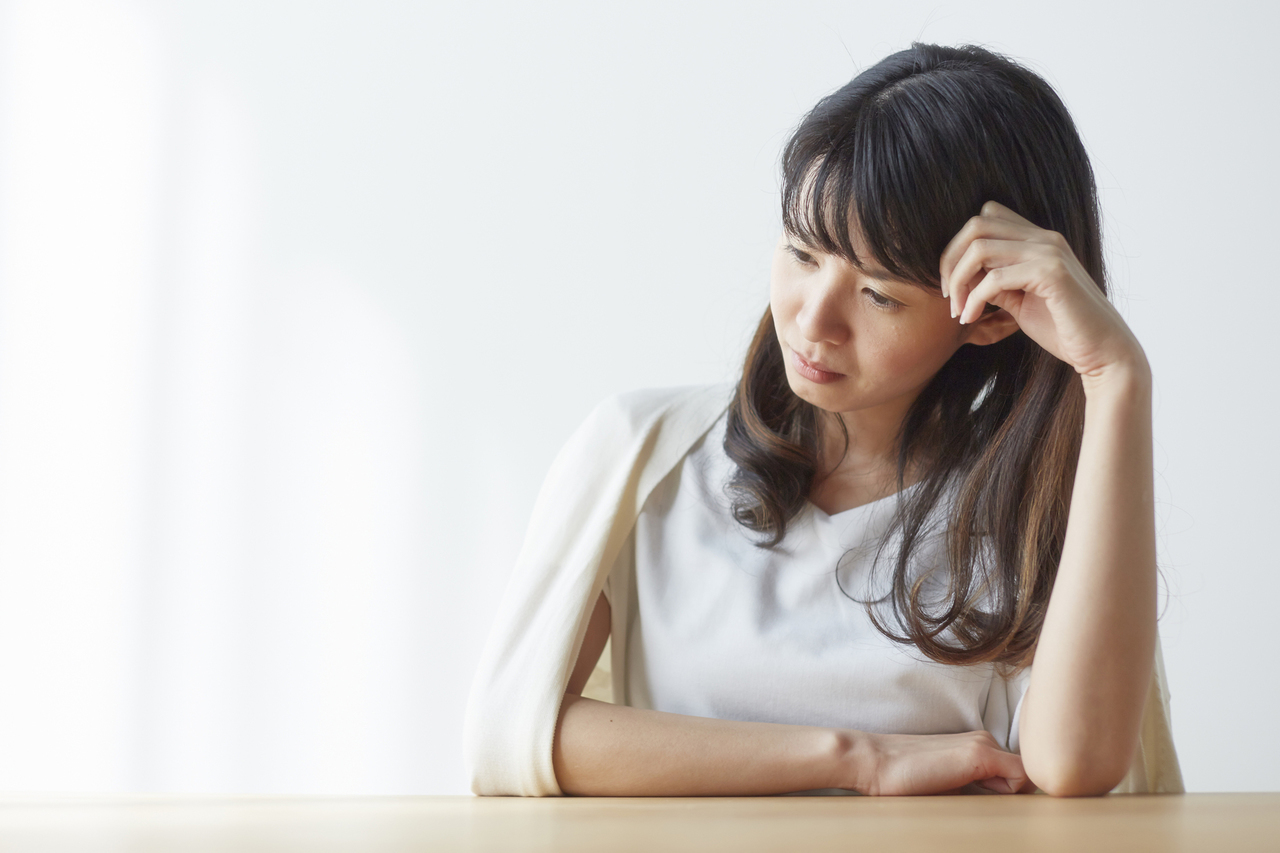 テーブルで肘をついて下を向く女性