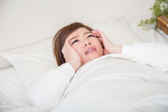 布団の中で両手をこめかみにあてて不安がっている女性